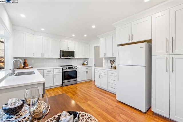 kitchen featuring sink, light hardwood / wood-style flooring, appliances with stainless steel finishes, white cabinets, and decorative backsplash