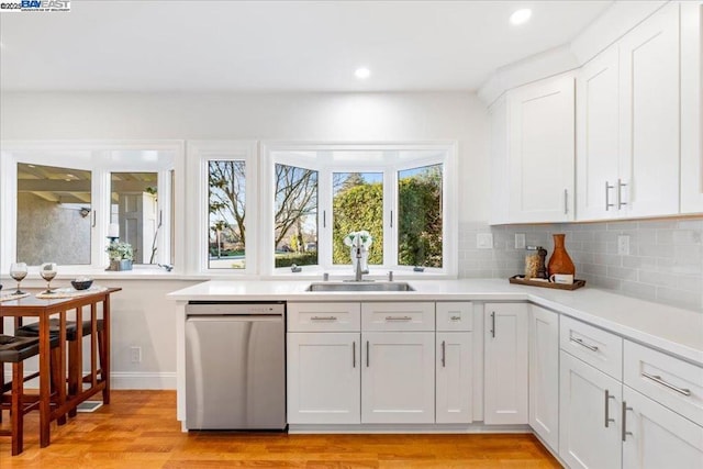 kitchen featuring sink, white cabinetry, stainless steel dishwasher, light hardwood / wood-style floors, and decorative backsplash