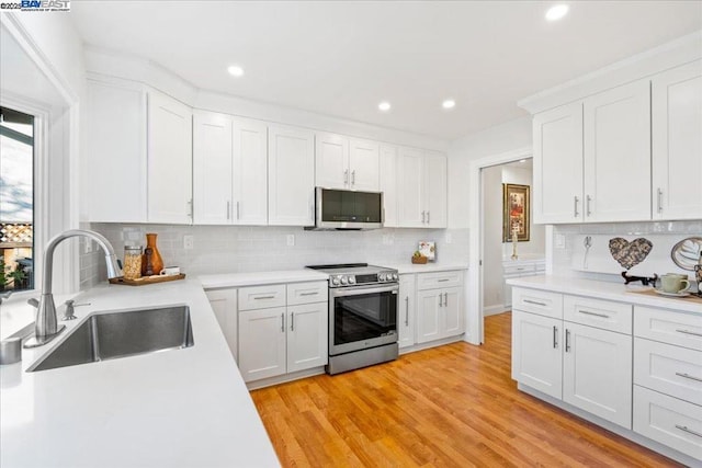 kitchen with sink, white cabinets, decorative backsplash, light hardwood / wood-style floors, and stainless steel appliances