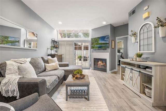 living area featuring light wood finished floors, visible vents, recessed lighting, and a glass covered fireplace