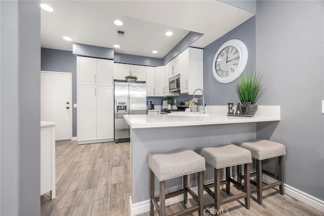 kitchen with sink, white cabinetry, appliances with stainless steel finishes, a kitchen breakfast bar, and kitchen peninsula