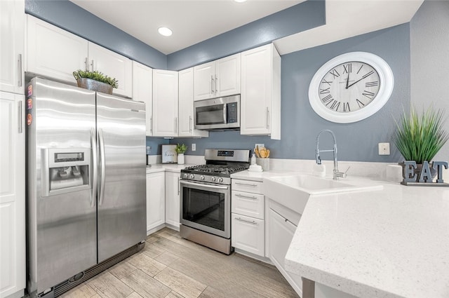 kitchen featuring light wood-type flooring, a sink, appliances with stainless steel finishes, white cabinets, and light stone countertops