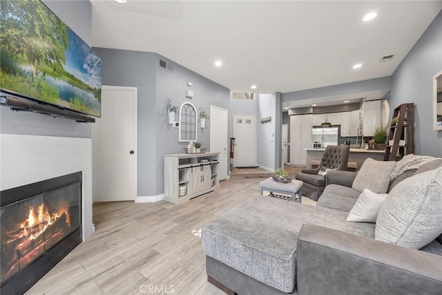 living room featuring a glass covered fireplace, light wood-style flooring, recessed lighting, and visible vents