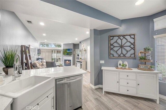 kitchen featuring stainless steel dishwasher, wood tiled floor, visible vents, and a sink