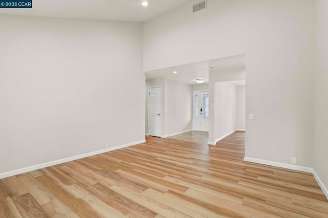 spare room with a towering ceiling and light wood-type flooring