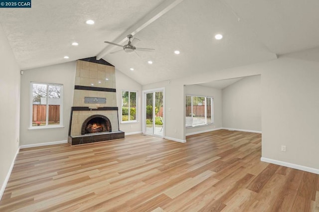 unfurnished living room with vaulted ceiling with beams, a wealth of natural light, a fireplace, and light hardwood / wood-style floors