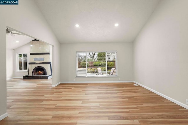 unfurnished living room with ceiling fan, vaulted ceiling, a tile fireplace, and light wood-type flooring