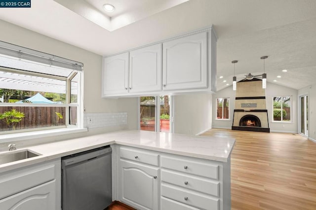 kitchen with dishwasher, white cabinets, a tiled fireplace, vaulted ceiling, and kitchen peninsula