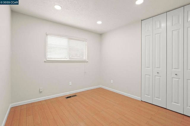 unfurnished bedroom featuring a textured ceiling, light wood-type flooring, and a closet