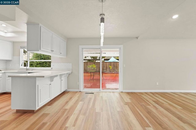 kitchen featuring hanging light fixtures, backsplash, white cabinets, and light wood-type flooring