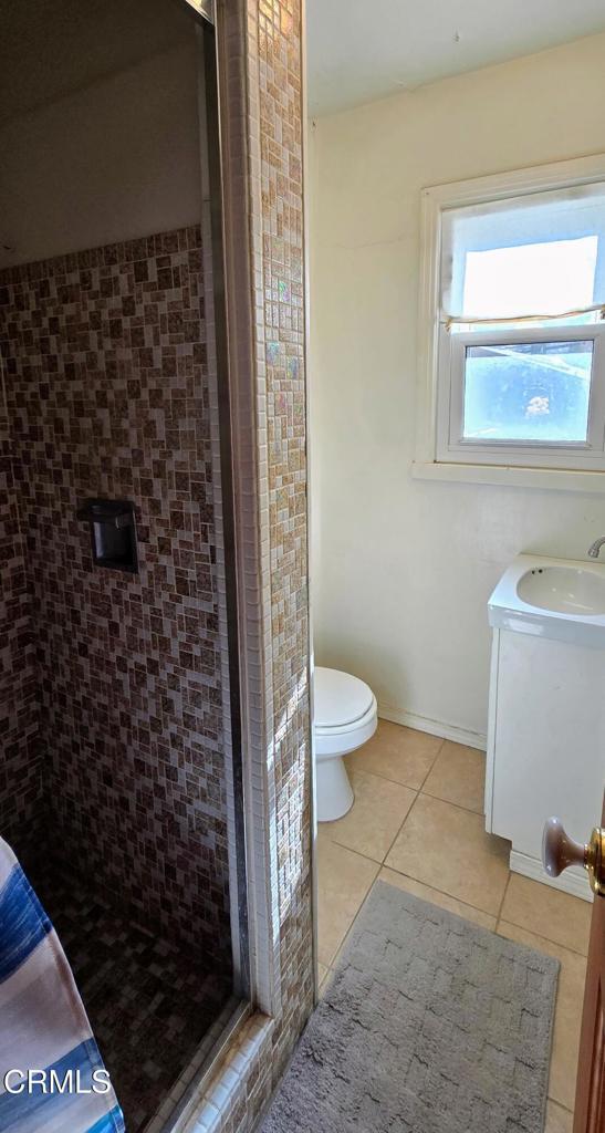 bathroom with tile patterned flooring, vanity, toilet, and a tile shower