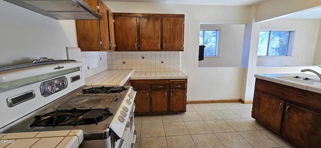 kitchen with sink, range with gas cooktop, exhaust hood, tile countertops, and backsplash