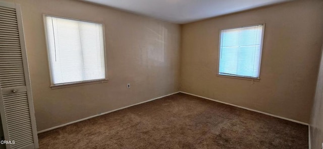 unfurnished room with a wealth of natural light and dark colored carpet