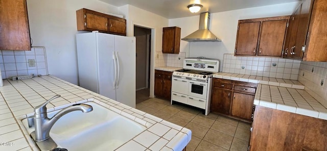 kitchen featuring light tile patterned flooring, backsplash, tile counters, wall chimney range hood, and white appliances