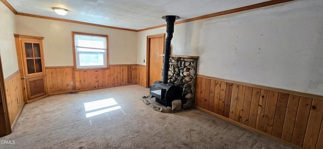 unfurnished living room with ornamental molding, wooden walls, light carpet, and a wood stove