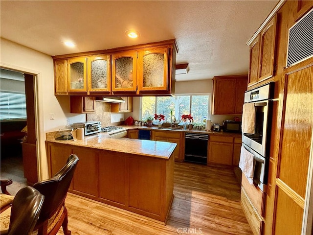 kitchen featuring black appliances, sink, light hardwood / wood-style floors, and kitchen peninsula