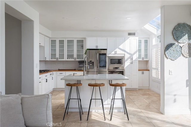 kitchen featuring a kitchen bar, stainless steel appliances, white cabinets, a center island with sink, and decorative backsplash