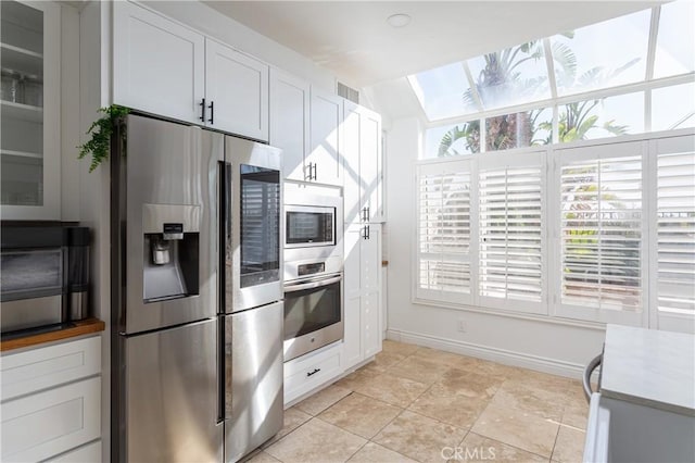 kitchen with stainless steel appliances, white cabinetry, lofted ceiling, and light tile patterned flooring