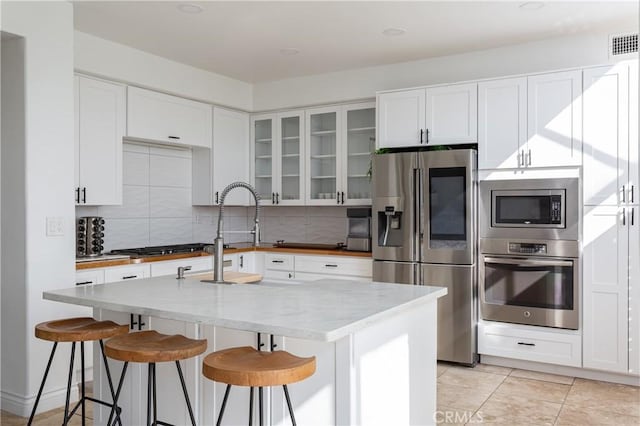 kitchen with white cabinetry, a kitchen bar, an island with sink, and appliances with stainless steel finishes