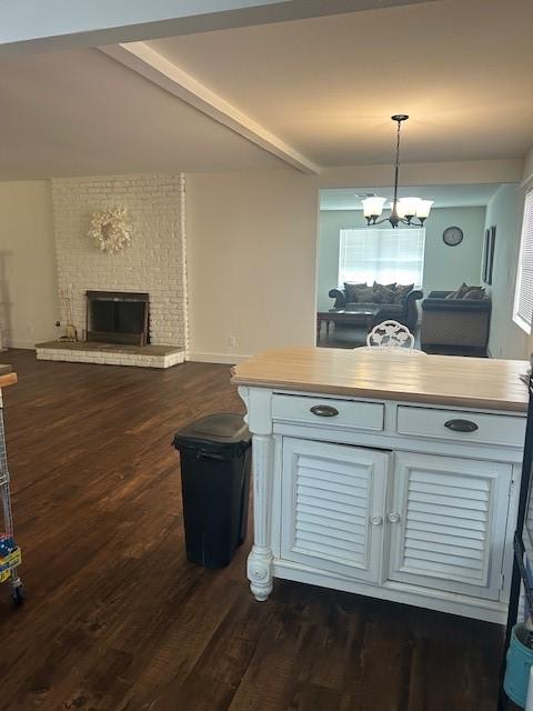 kitchen with vaulted ceiling with beams, dark hardwood / wood-style floors, a brick fireplace, decorative light fixtures, and a chandelier