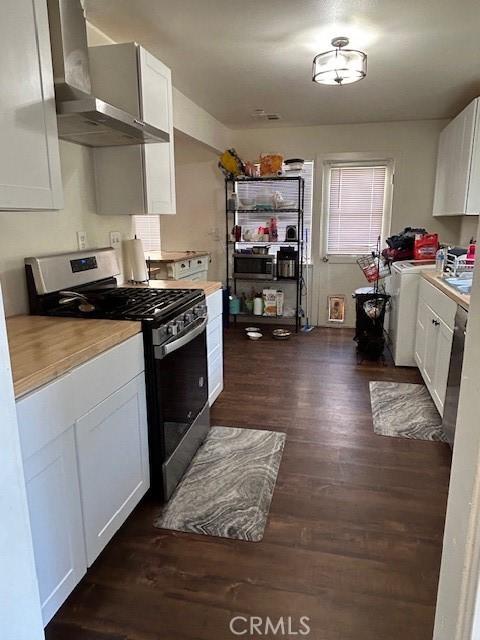 kitchen featuring stainless steel gas range, dark hardwood / wood-style floors, white cabinets, washer / dryer, and wall chimney exhaust hood