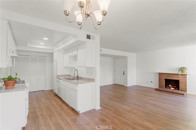 kitchen with sink, decorative light fixtures, a brick fireplace, light hardwood / wood-style floors, and white cabinets