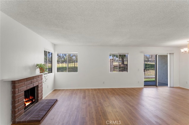 unfurnished living room with a chandelier, a textured ceiling, a fireplace, and light hardwood / wood-style floors