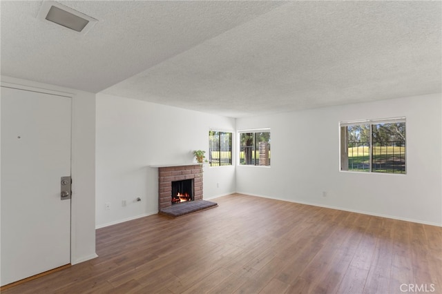 unfurnished living room with hardwood / wood-style flooring, a brick fireplace, and a textured ceiling