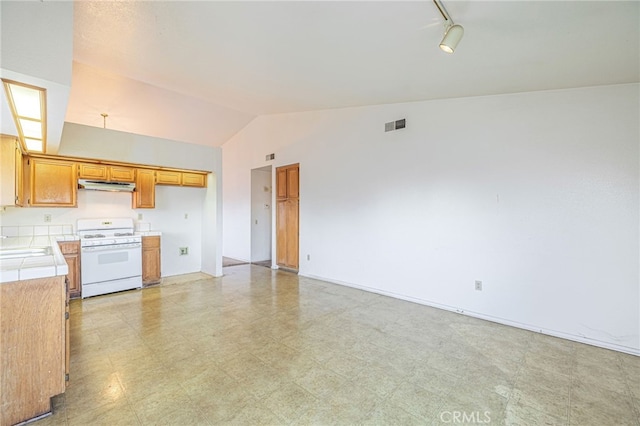 kitchen with white gas range, sink, tile countertops, and lofted ceiling