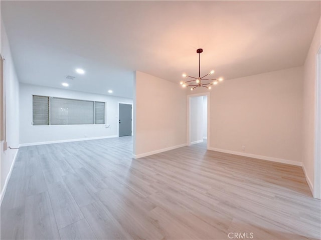 spare room featuring light hardwood / wood-style floors and a notable chandelier