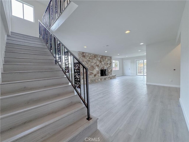 staircase with wood-type flooring and a stone fireplace