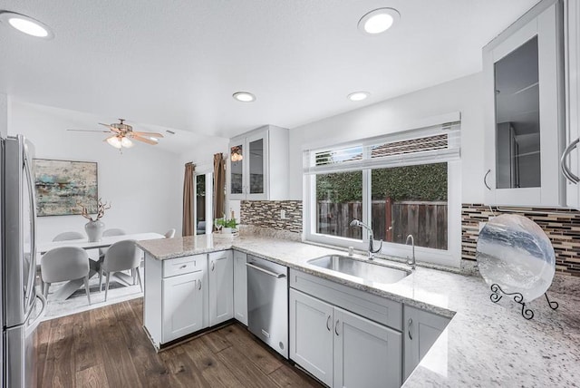 kitchen featuring sink, light stone counters, kitchen peninsula, stainless steel appliances, and dark wood-type flooring