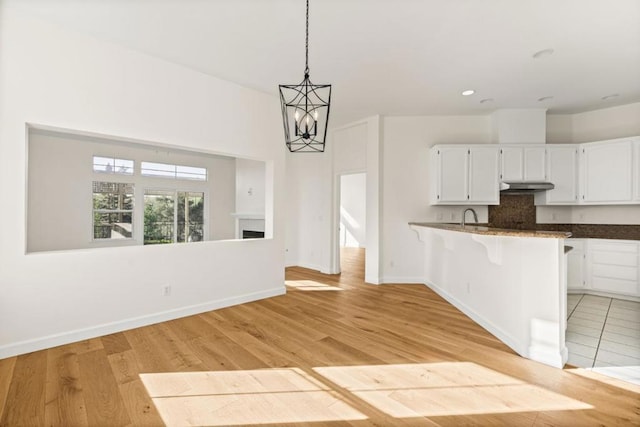 kitchen featuring a kitchen bar, white cabinetry, decorative light fixtures, kitchen peninsula, and light hardwood / wood-style floors