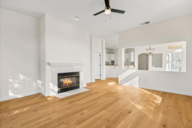 unfurnished living room with a tiled fireplace, ceiling fan with notable chandelier, and light wood-type flooring