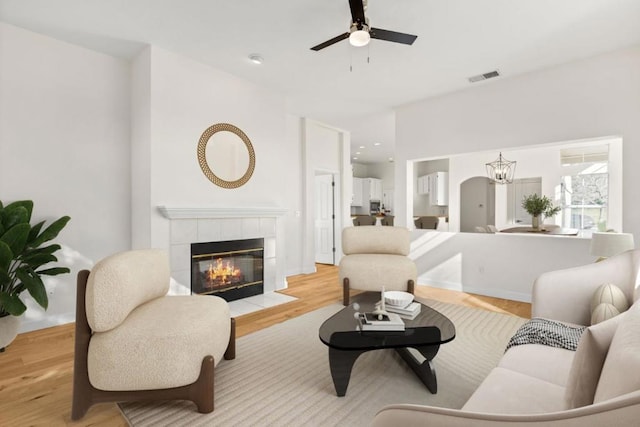 living room with a tile fireplace, ceiling fan with notable chandelier, and light hardwood / wood-style flooring