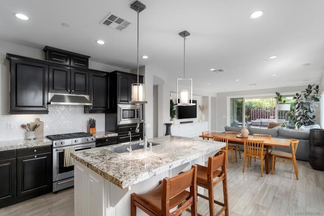 kitchen featuring pendant lighting, sink, a breakfast bar, stainless steel appliances, and an island with sink