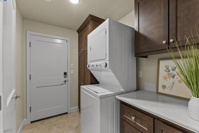 clothes washing area with cabinets, light tile patterned flooring, and stacked washer / drying machine