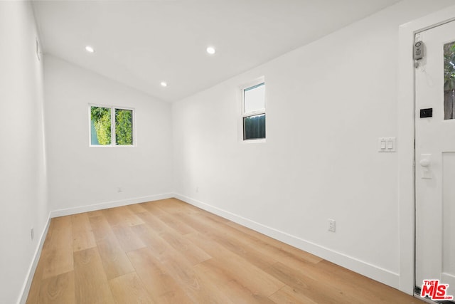 spare room with lofted ceiling and light wood-type flooring