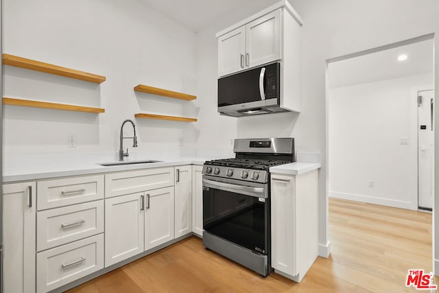 kitchen with stainless steel appliances, white cabinetry, sink, and light hardwood / wood-style flooring