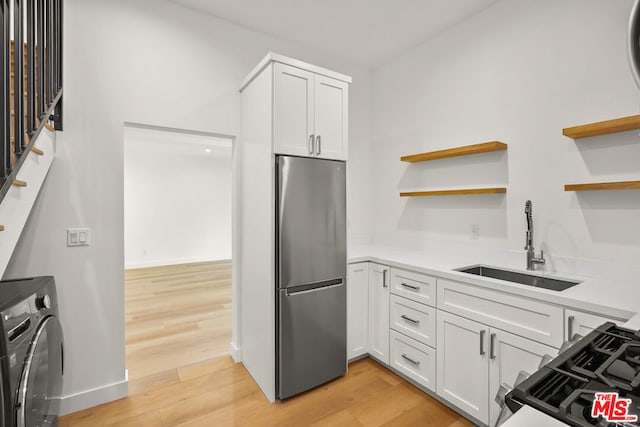 kitchen with sink, stainless steel fridge, light hardwood / wood-style floors, white cabinets, and washer / clothes dryer