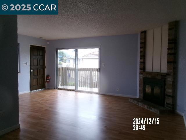 unfurnished living room with hardwood / wood-style flooring, a brick fireplace, and a textured ceiling