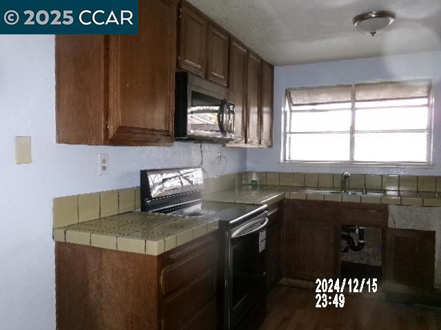 kitchen with dark wood-type flooring, tile counters, sink, and electric range