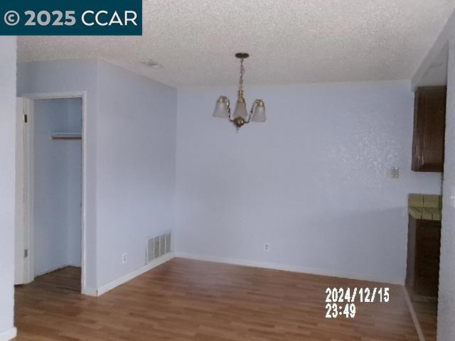 unfurnished dining area featuring hardwood / wood-style floors, a notable chandelier, and a textured ceiling