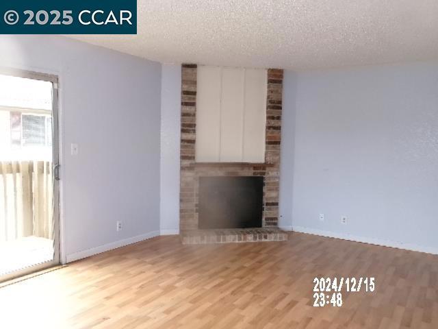 unfurnished living room featuring light hardwood / wood-style flooring, a brick fireplace, and a textured ceiling