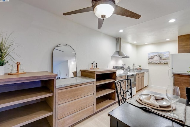 kitchen featuring wall chimney range hood, white appliances, light hardwood / wood-style flooring, sink, and ceiling fan