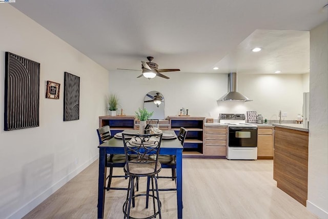 kitchen featuring wall chimney range hood, white electric range, ceiling fan, light hardwood / wood-style floors, and light brown cabinets