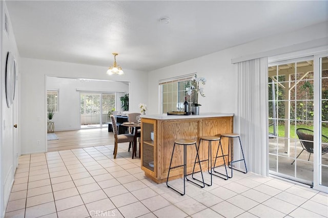 kitchen with pendant lighting, a kitchen bar, light tile patterned floors, kitchen peninsula, and an inviting chandelier