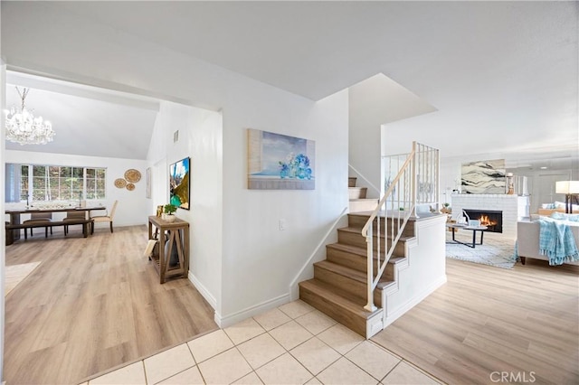 staircase featuring hardwood / wood-style flooring, vaulted ceiling, a brick fireplace, and a notable chandelier