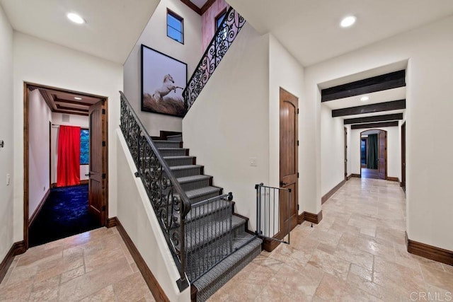 stairway with stone tile floors, arched walkways, baseboards, beam ceiling, and recessed lighting