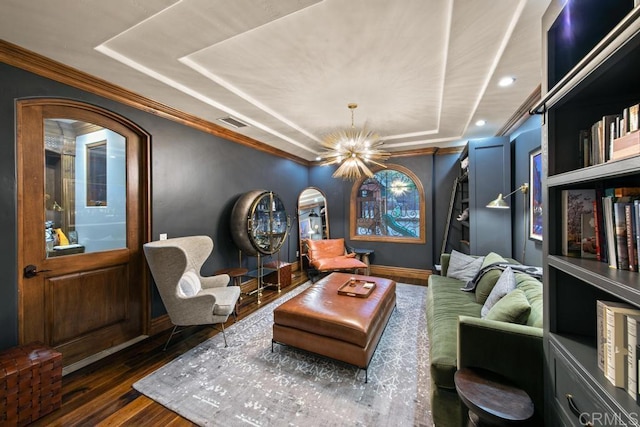 living area with crown molding, wood finished floors, visible vents, a raised ceiling, and an inviting chandelier